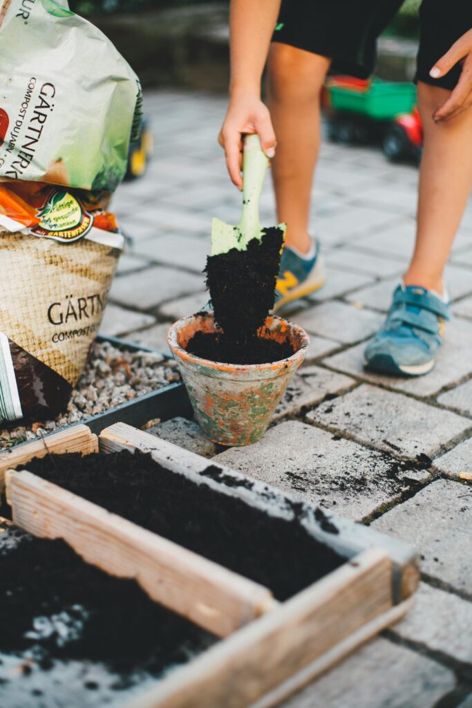 boy in black shorts shoveling soil into a gardening pot