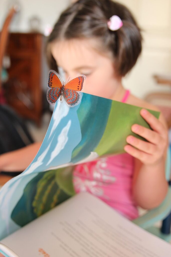 little girl reading a book with a butterfly on the corner of the page