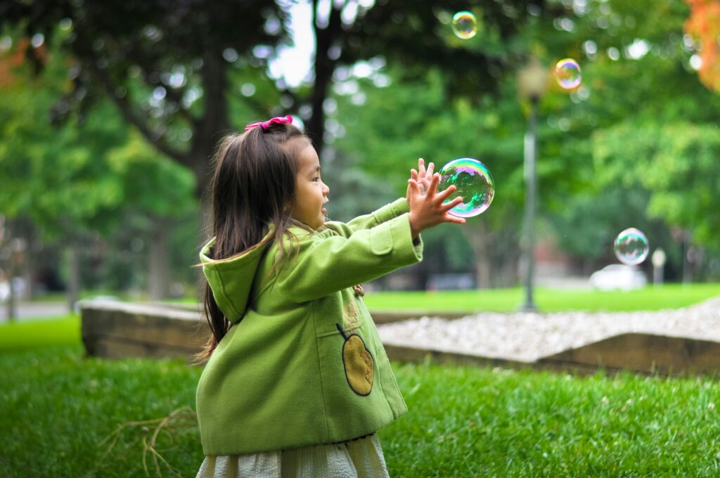 girl in green jacket chasing bubbles in the park