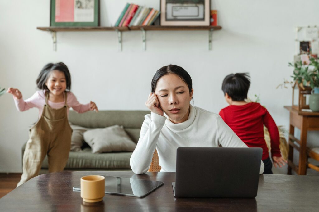 mom frustrated on computer as kids have fun and run In the background