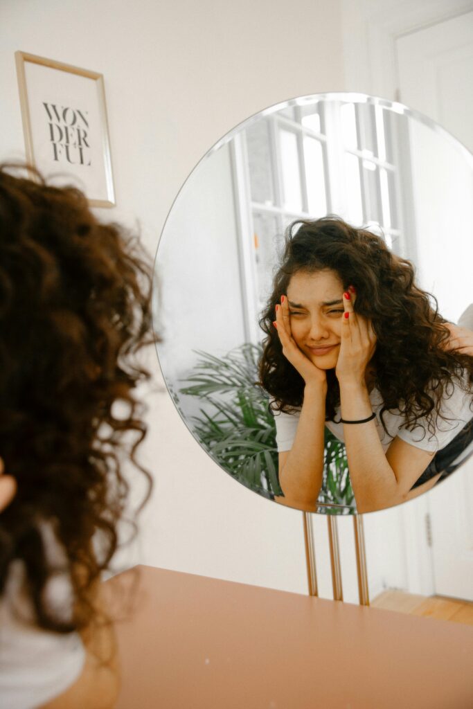 distressed woman looking in mirror with hands over her face