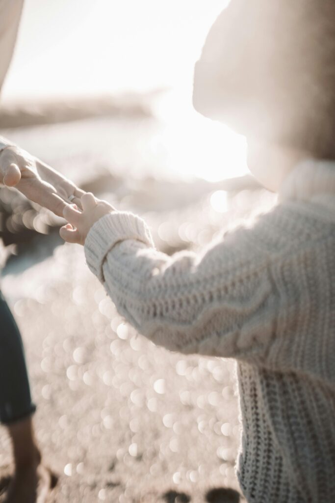 child in knit sweater holding parent's hand as the sun rises in the distance