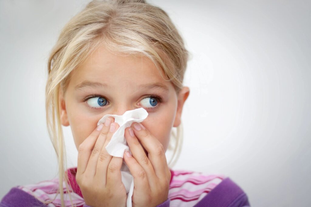 child dealing with seasonal allergies holding a tissue over her nose